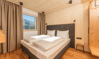A modern bedroom with a double bed and a light wood design. Large windows offer a view of the surroundings.