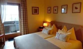 A cozy bedroom with two single beds and warm colors. The windows offer a view of a small balcony and harmonious wall paintings.