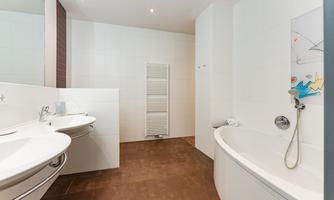A modern bathroom with two sinks, a bathtub, and a towel radiator. The walls are covered with bright tiles, which creates a clean and spacious impression.