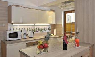 A modern kitchen with wooden surfaces and a spacious work area. Fresh fruit and a bottle of wine are on the countertop.