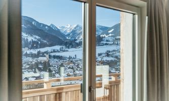 A beautiful view through a window of snow-covered mountains and a small village. The sun shines on the picturesque winter landscape.