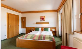 A cozy bedroom with a double bed and colorful pillows. There are wooden paneling and a friendly, bright room.