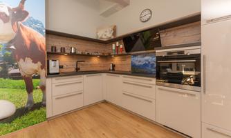 A modern kitchen with bright cabinets and wooden shelves. On the wall, there are pictures of mountains and cows.