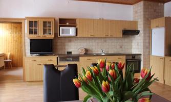 A modern kitchen with wooden furniture and a stainless steel sink. A bouquet of colorful tulips is on the table.