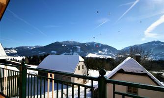 A snowy landscape with mountains in the background and a clear blue sky. Balloons are floating above the mountains.