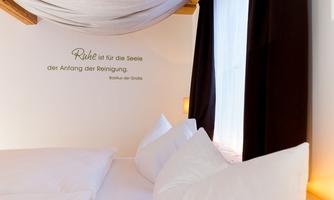A cozy bedroom with a central bed and pillows. An inspiring quote about peace is on the wall.