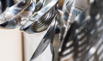 A variety of shiny cooking utensils hang on a wall. The silver spoons and ladles reflect the light.