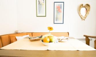 A bright dining area with a wooden table and orange chairs. There is a bowl of fruit and a sunflower in a vase on the table.