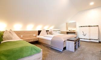 A modern room with two beds and a comfortable sofa bed. The decor is bright and cheerful with natural wood tones.
