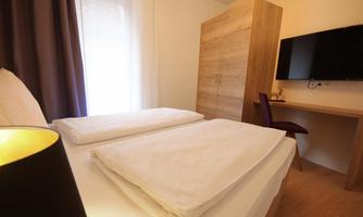 A cozy bedroom with a large double bed and minimalist design. There is a desk and a television on the wall.
