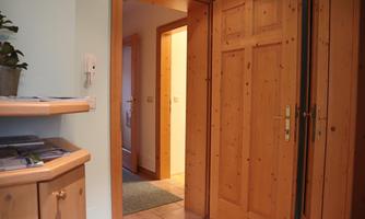 A bright hallway with wooden paneling and open doors. On the left side, there is a piece of furniture with a plant.