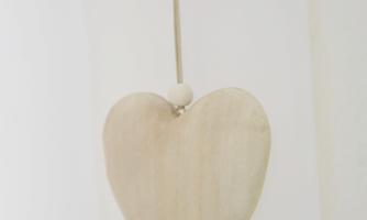 A hanging wooden heart on a white wall. It is simple and unpainted, with a small wooden bead on top.