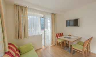 A bright living room with a sofa and a dining table. Large windows provide plenty of daylight.