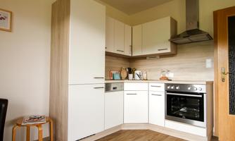 A modern kitchen with white cabinets and wooden details. The room is well-lit and features a stove and a sink.