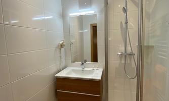 A modern bathroom with a shower and a sink under a mirror. The walls are tiled in light colors and the floor is kept neutral.
