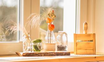 A bright windowsill with decorative glasses and dried flowers. Wooden accessories add a warm atmosphere to the scene.