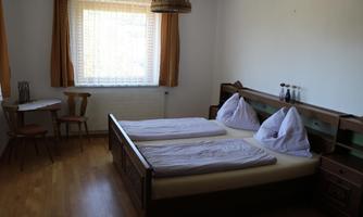 A simple bedroom with two beds and wooden furniture. There is a small table and a window with daylight.