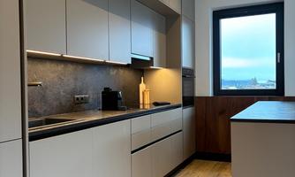 A modern kitchen with gray cabinets and a wooden floor. A large window lets in natural light.
