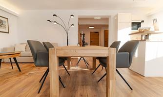A modern dining area with a large wooden table and elegant chairs. The decor is bright and inviting, with wooden flooring and natural light.