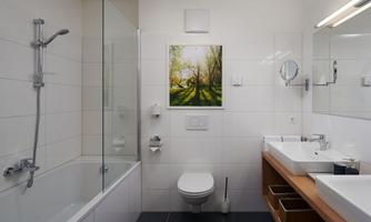 A modern bathroom with a bathtub and a wooden sink. On the wall hangs a picture of a tree with sun rays.