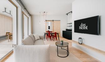 A modern living room with a beige sofa and a round table. A television hangs on the wall with the inscription "that stays."