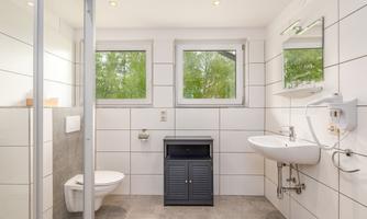 A modern bathroom with bright tiles and large windows. There is a shower, a sink, and a toilet.