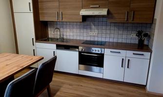 A modern kitchen with wooden and white elements. It includes a stove, a sink, and a table with chairs.