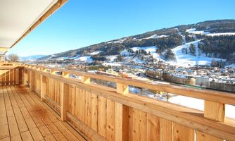 A beautiful view from a balcony of a snowy mountain landscape. The clear blue sky and the wooden structure of the balcony create a cozy atmosphere.