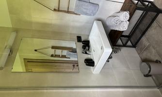 A modern bathroom with a white sink, a large mirror, and towels. The space features gray tiles and a stylish storage unit.