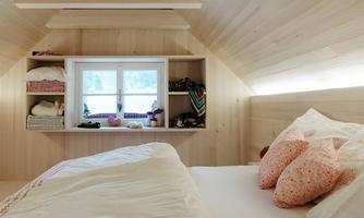 A cozy bedroom with wooden paneling and a large window. On the bed, there are pillows in soft colors and a fresh duvet.