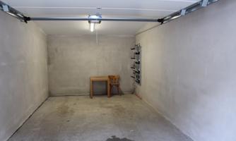 An empty garage with smooth, gray walls. A simple table and a workbench are in the room.