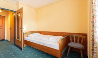 A simple room with a single bed and a chair. The walls are painted yellow, and the carpet has a green pattern.