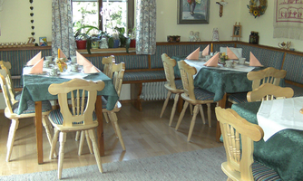 A cozy restaurant with wooden tables and chairs. The tables are decorated and there are large windows that let in a lot of light.