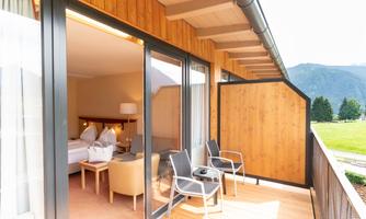 A modern room with a balcony that offers a view of nature. The balcony is furnished with chairs and a table.