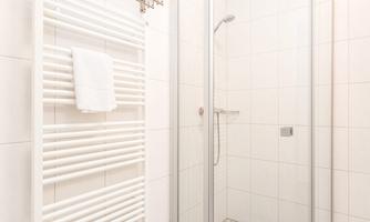 A modern shower with glass partition and white tiles. Towels hang on a radiator.