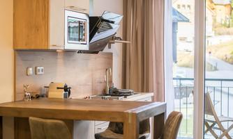A modern kitchen unit with a wooden chair and a dining table. There is a view of the surroundings through the window.