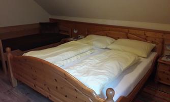 A cozy bedroom with a large wooden double bed and a single bed next to it. The room walls are slanted and the floor is covered with a carpet.
