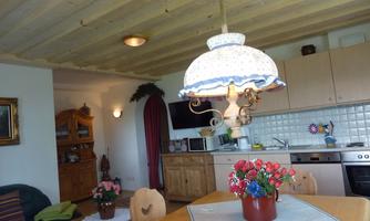 A cozy kitchen with a wooden table and a decorative lamp. On the table, there is a flower pot with colorful flowers.