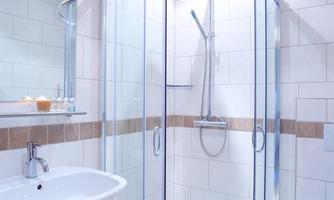 A modern bathroom with a glass shower and a sink. The walls are tiled in light colors and a mirror is present.