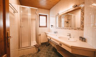 A modern bathroom with a shower and a large mirror.  
Bright tiles and a wooden ceiling create a cozy atmosphere.