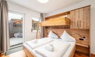 A modern bedroom with a wooden bed and two cozy beds. The room has large windows and access to a small outdoor area.