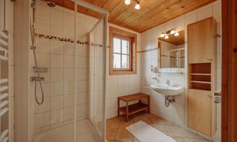 A modern bathroom with a shower and wooden ceiling. The walls are tiled and there is a sink area with a mirror.