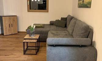 A modern living room with a gray couch and a small table.  
On the wall hangs a picture of a tree, and there is a view outside the window.