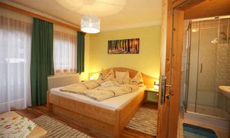 A cozy bedroom with a double bed and soft colors. In the background, there is a bathroom with a shower.