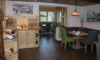 A cozy room with wooden furniture and modern colors. Breakfast items are ready on a buffet, and there are dining areas with tables and chairs.
