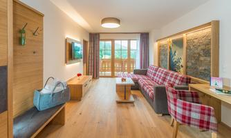 A cozy living room with wooden details and a large window. The decor is modern and welcoming, featuring a comfortable sofa and a dining table.