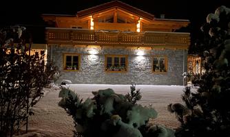 A beautiful chalet in the snow at night. The facade is illuminated and looks inviting.
