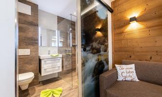 A modern bathroom with a shower cabin and wooden paneling. Next to the bathroom is a cozy sofa with a decorative pillow.