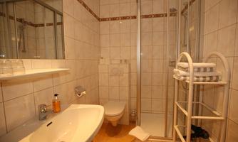A small bathroom with a shower, a sink, and a toilet. The walls are tiled in light colors and there is a towel rack.