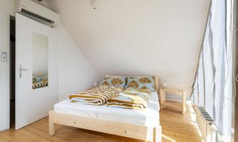 A bright bedroom with a wooden bed and colorful bedding. A mirror and a chair complement the cozy atmosphere.